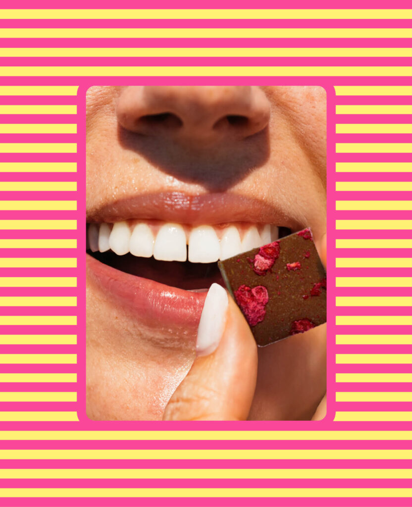 A woman biting a piece of Kelsi's brownie batter bite over top of a striped background.