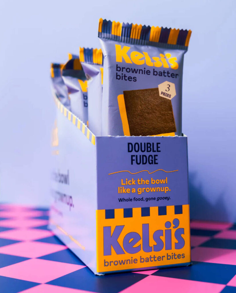 Kelsi's brownie batter bites in a vibrant orange and purple box over top of a checkered table.