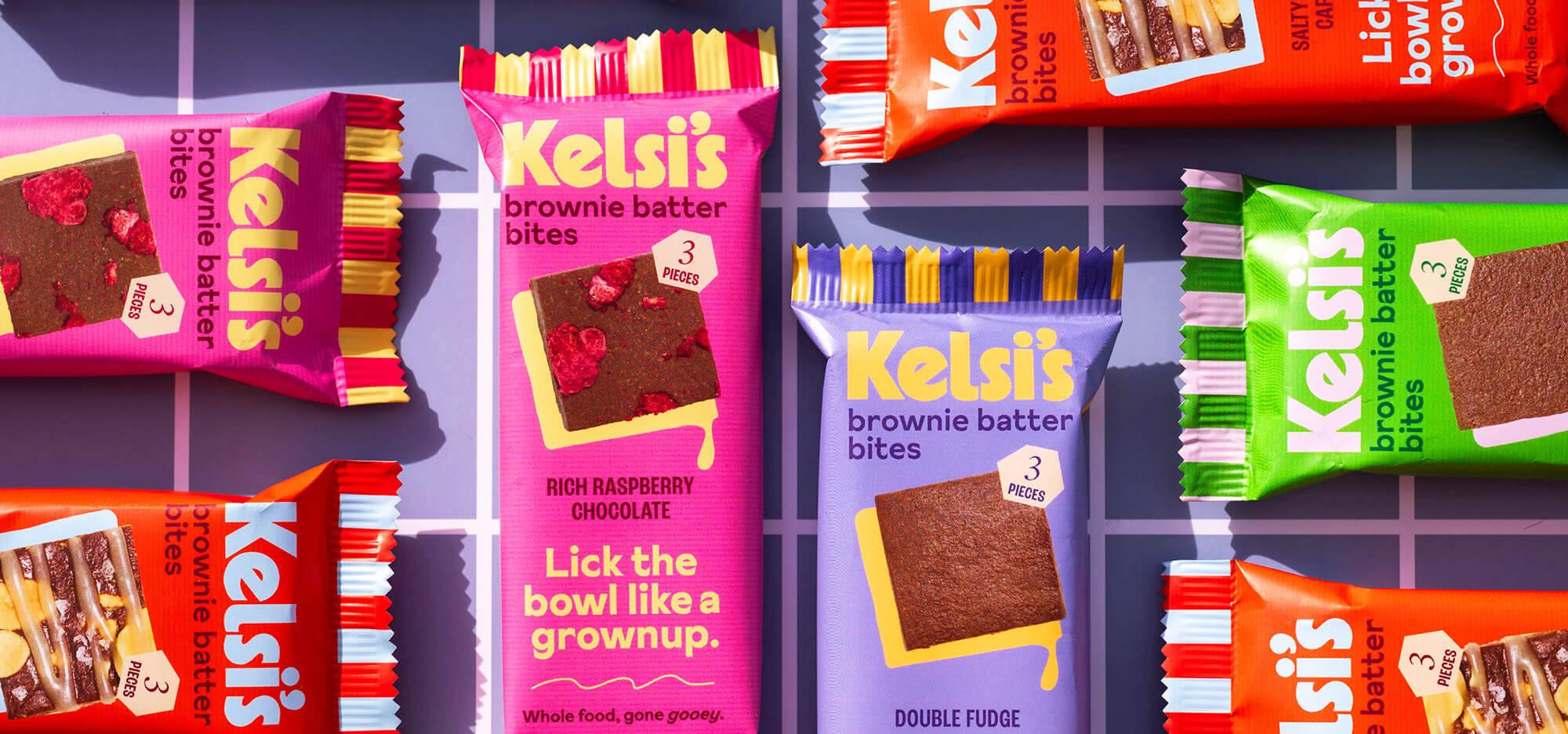 Multiple flavors of Kelsi's brownie bites arranged in perpendicular patterns on a checkerboard patterned surface.