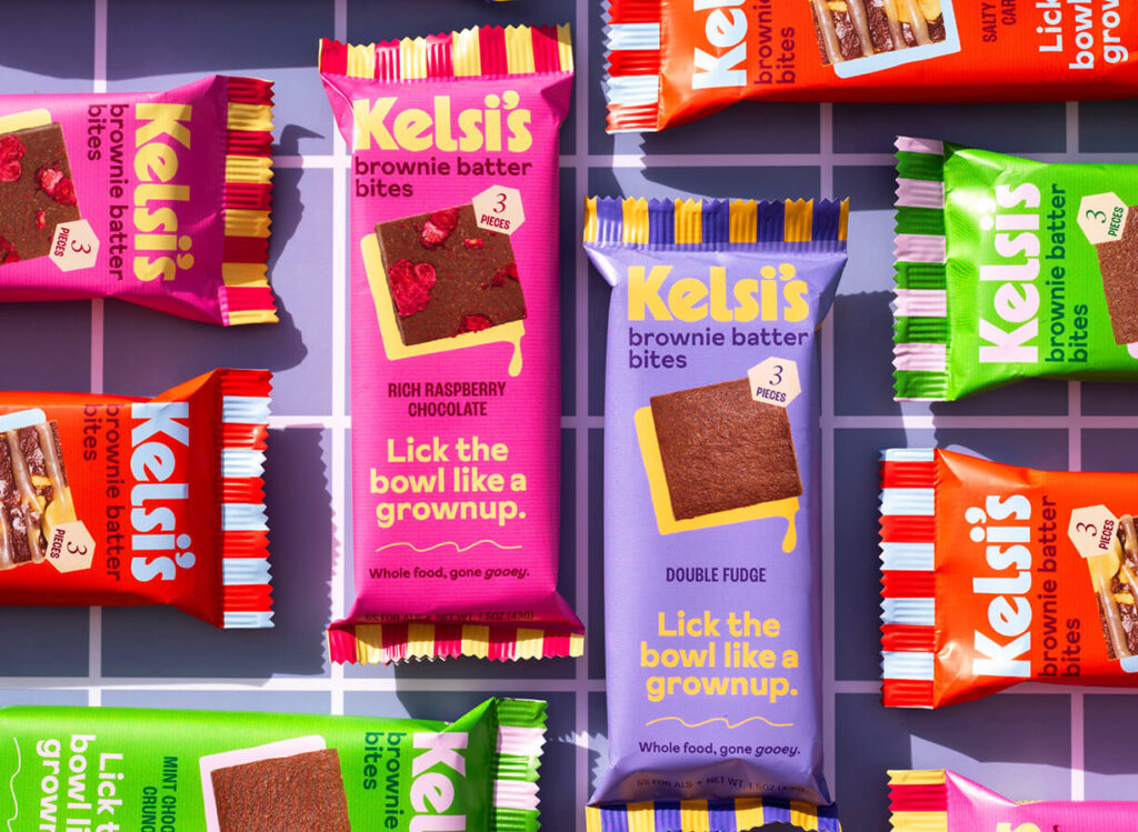 Multiple flavors of Kelsi's brownie bites arranged in perpendicular patterns on a checkerboard patterned surface.