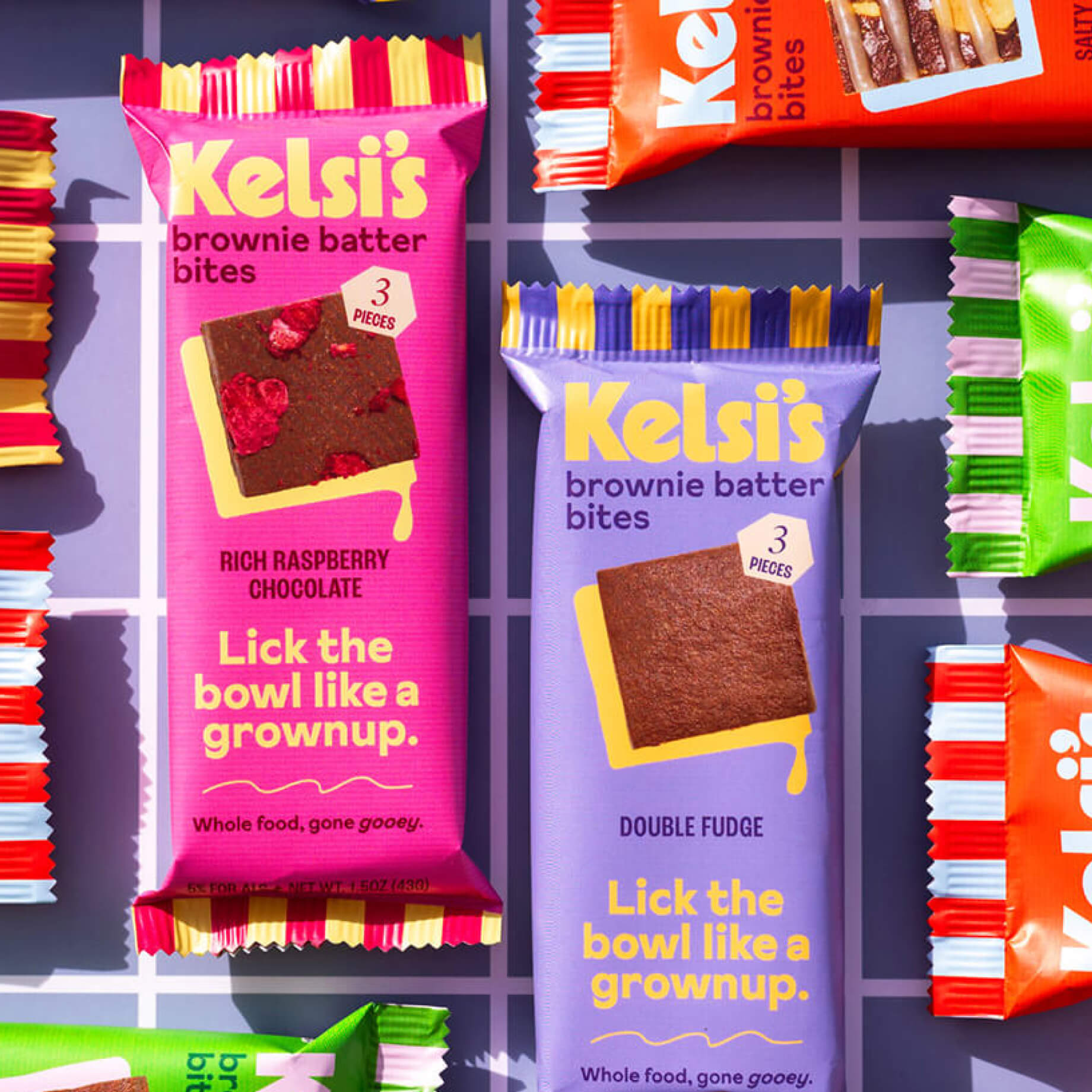 Multiple flavors of Kelsi's brownie bites arranged in perpendicular patterns on a checkerboard patterned surface.