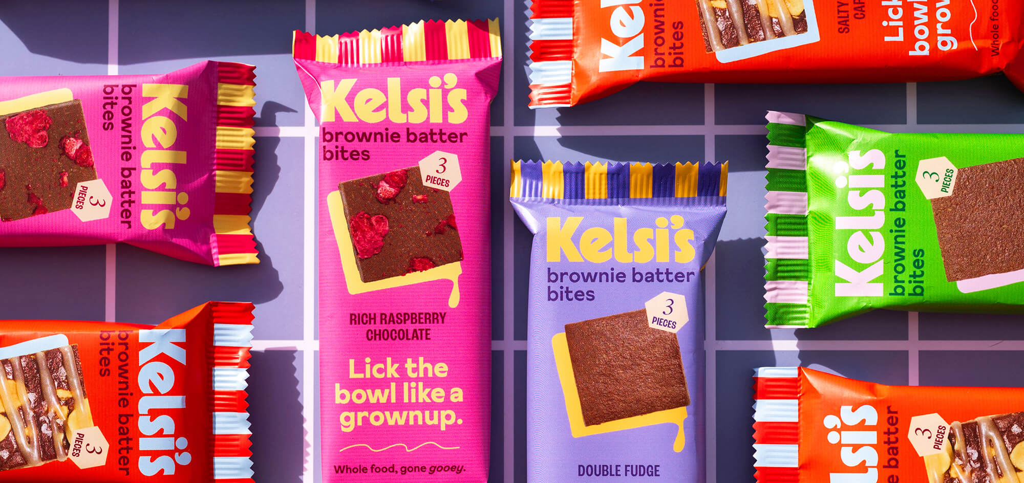 Multiple flavors of Kelsi's brownie bites arranged in perpendicular patterns on a checkerboard patterned surface.
